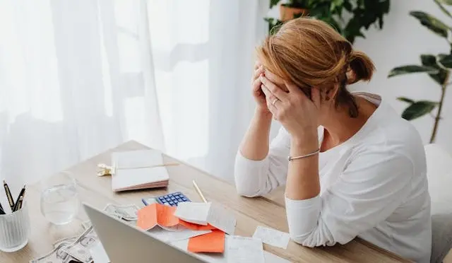 Người phụ nữ ôm đầu mệt mỏi bên đống hóa đơn và máy tính vì gặp lỗ hổng tài chính