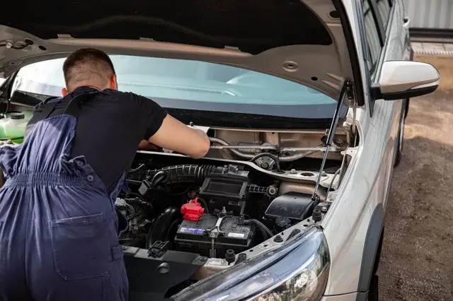 Người thợ sửa xe đang kiểm tra và bảo dưỡng các chi tiết kỹ thuật bên trong khoang máy của một chiếc ô tô