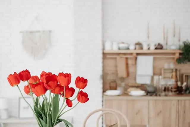 Một bình hoa mộc mạc được cắm gọn gàng đặt trên bàn ăn gỗ trong căn bếp ấm cúng
