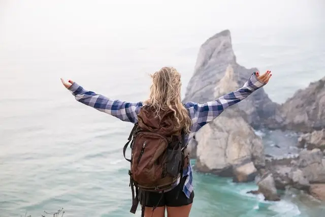 Cô gái đeo balo đứng trên đỉnh núi cao dang rộng hai tay